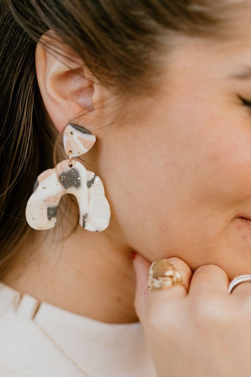 Close side view of model wearing the Once Upon A Time Earrings that feature mauve, cream and black marbled geometric pendants with gold speckles.