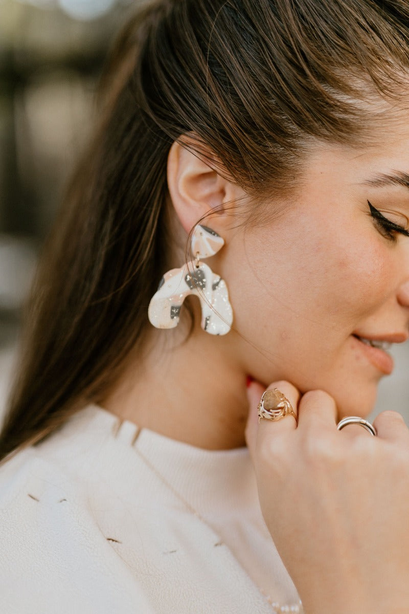 Close side view of model wearing the Once Upon A Time Earrings that feature mauve, cream and black marbled geometric pendants with gold speckles.