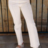Front view of model wearing the Remi Off White Cropped Pants which features cream denim knit fabric, light brown stitch details, exterior front lining, cropped legs, two front pockets, two back pockets, belt loops and front zipper with button closure.