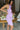 Close up side view of model wearing the Out And About Dress In Lavender which features lavender knit fabric, ruched side details, midi length, lavender lining, a round neckline and a sleeveless design.