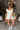 Full body view of model wearing the Modern Day Ruffle Romper which features cream fabric, pockets on each side, front zipper closure, square neckline, ruffle straps, elastic band in the back and sleeveless.