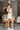 Full body side view of model wearing the Modern Day Ruffle Romper which features cream fabric, pockets on each side, front zipper closure, square neckline, ruffle straps, elastic band in the back and sleeveless.