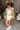 Side view of model wearing the Modern Day Ruffle Romper which features cream fabric, pockets on each side, front zipper closure, square neckline, ruffle straps, elastic band in the back and sleeveless.