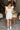 Full body back view of model wearing the Modern Day Ruffle Romper which features cream fabric, pockets on each side, front zipper closure, square neckline, ruffle straps, elastic band in the back and sleeveless.