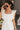 Close up view of model wearing the Modern Day Ruffle Romper which features cream fabric, pockets on each side, front zipper closure, square neckline, ruffle straps, elastic band in the back and sleeveless.
