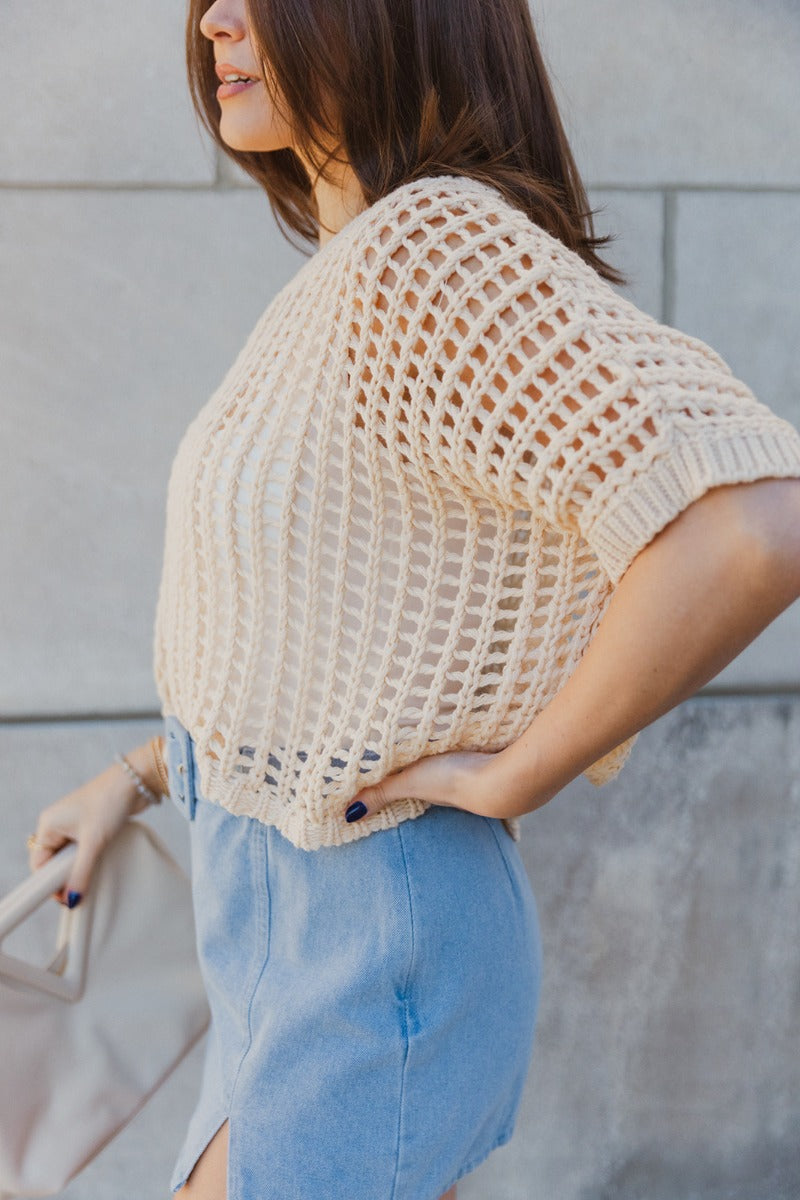 Side view of model wearing the Helen Beige Open Knit Top which features beige open knit fabric, thick hem, round neckline and short sleeves.