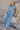 Full body view of model wearing the Everly Chambray Blue Halter Neckline Jumpsuit which features light blue lightweight fabric, pleated details, two front slit pockets, wide pant legs, light blue shorts lining, a halter neckline with a twist detail, a sle