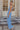 Side view of model wearing the Everly Chambray Blue Halter Neckline Jumpsuit which features light blue lightweight fabric, pleated details, two front slit pockets, wide pant legs, light blue shorts lining, a halter neckline with a twist detail, a sleevele