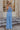 Full body back view of model wearing the Everly Chambray Blue Halter Neckline Jumpsuit which features light blue lightweight fabric, pleated details, two front slit pockets, wide pant legs, light blue shorts lining, a halter neckline with a twist detail,