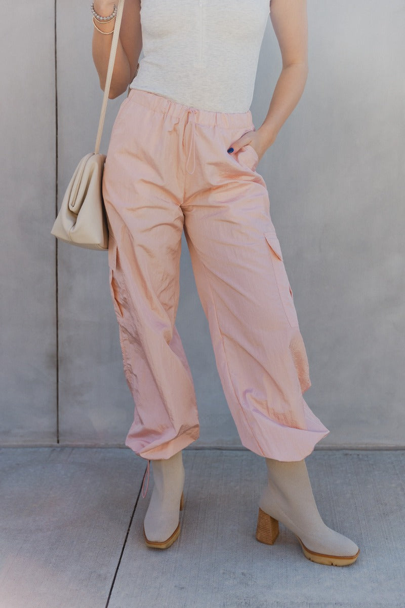 Front view of model wearing the Harper Blush Cargo Drawstring Pants which features blush nylon fabric, two front slit pockets, two side cargo pockets, elastic waistband with drawstring and wide pant legs with drawstring at ankles.