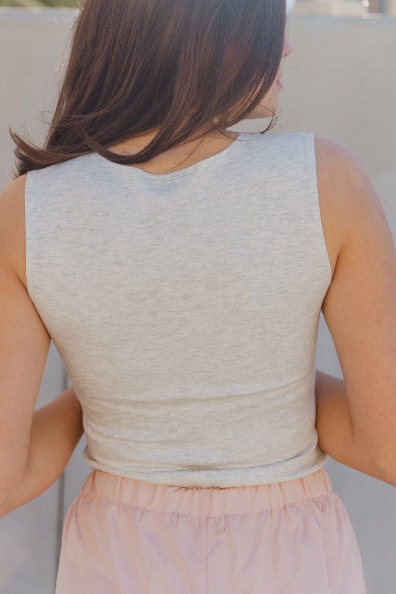 Back view of model wearing the Isla Heather Grey Zip Up Sleeveless Bodysuit which features light heather grey knit fabric, a monochrome front zip up, a round neckline, a sleeveless body, and a thong bottom with snap closures.