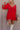 Front view of model wearing the Rowyn Red Short Sleeve Dress which features red rayon fabric, three tiered body style, ruffle hem, mini length, red lining, smocked waist, v-neckline with tie closure and short puff sleeves.