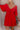 Close up view of model wearing the Rowyn Red Short Sleeve Dress which features red rayon fabric, three tiered body style, ruffle hem, mini length, red lining, smocked waist, v-neckline with tie closure and short puff sleeves.