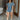 Full body front view of model wearing the Denim Dreams Romper that has light wash denim fabric, two front pockets, an elastic waistband, a front zipper closure, a plunge neckline and short sleeves