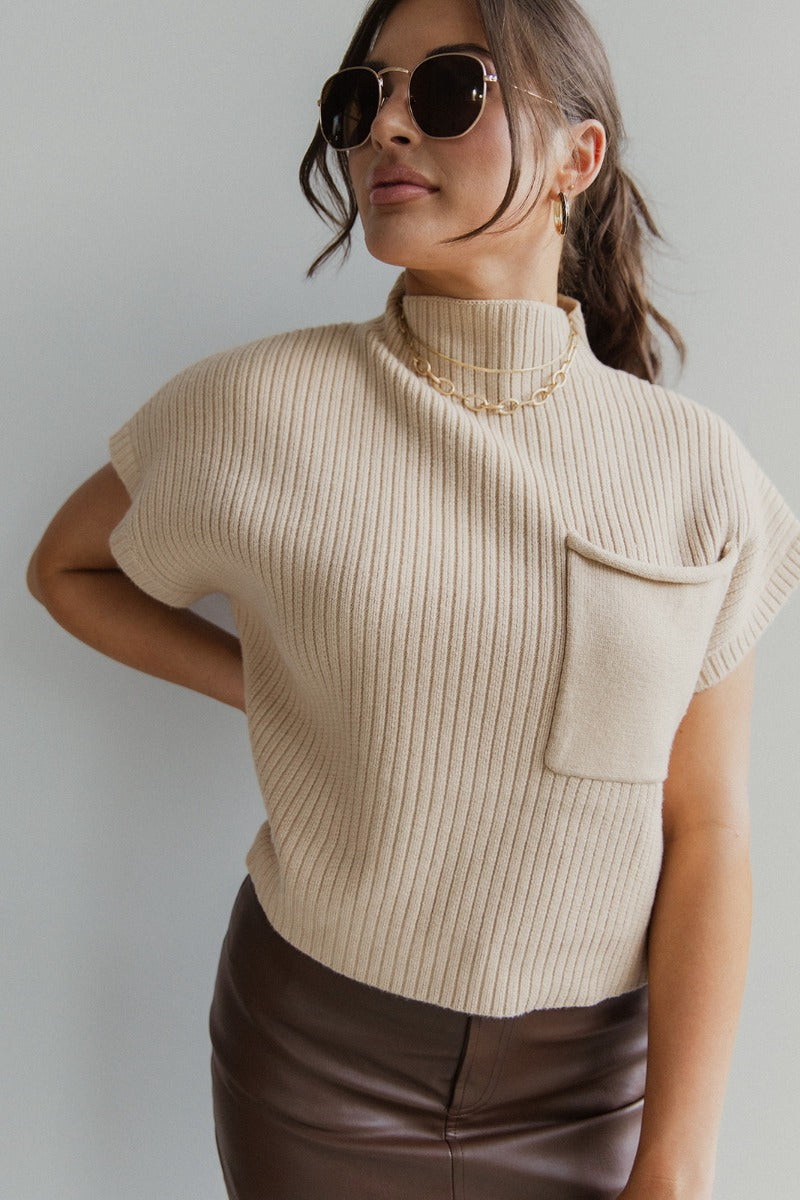 front view of model wearing the Ready For It Mock Neck Top that has tan cable knit fabric, a cropped waist, one front chest pocket, a mock neck and short sleeves
