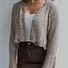 
Front view of model wearing the Simply The Vibe Cardigan which features cream and brown knit fabric, distressed details, a cropped waist, covered button-up closures, a round neckline and long flare sleeves. The cardigan is open.