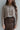 
Front view of model wearing the Simply The Vibe Cardigan which features cream and brown knit fabric, distressed details, a cropped waist, covered button-up closures, a round neckline and long flare sleeves. The cardigan is closed.