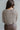 Back view of model wearing the Simply The Vibe Cardigan which features cream and brown knit fabric, distressed details, a cropped waist, covered button-up closures, a round neckline and long flare sleeves.
