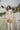 Frontal view of the More Than Enough Romper that features an ivory corduroy material, a collar neck, a surplice front, a long sleeve with a button, a front zipper, pockets, and pleating on the legs