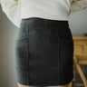 Front view of The All American Skirt In Charcoal features charcoal grey knit fabric, two front pockets, mini length, and back zipper closure.