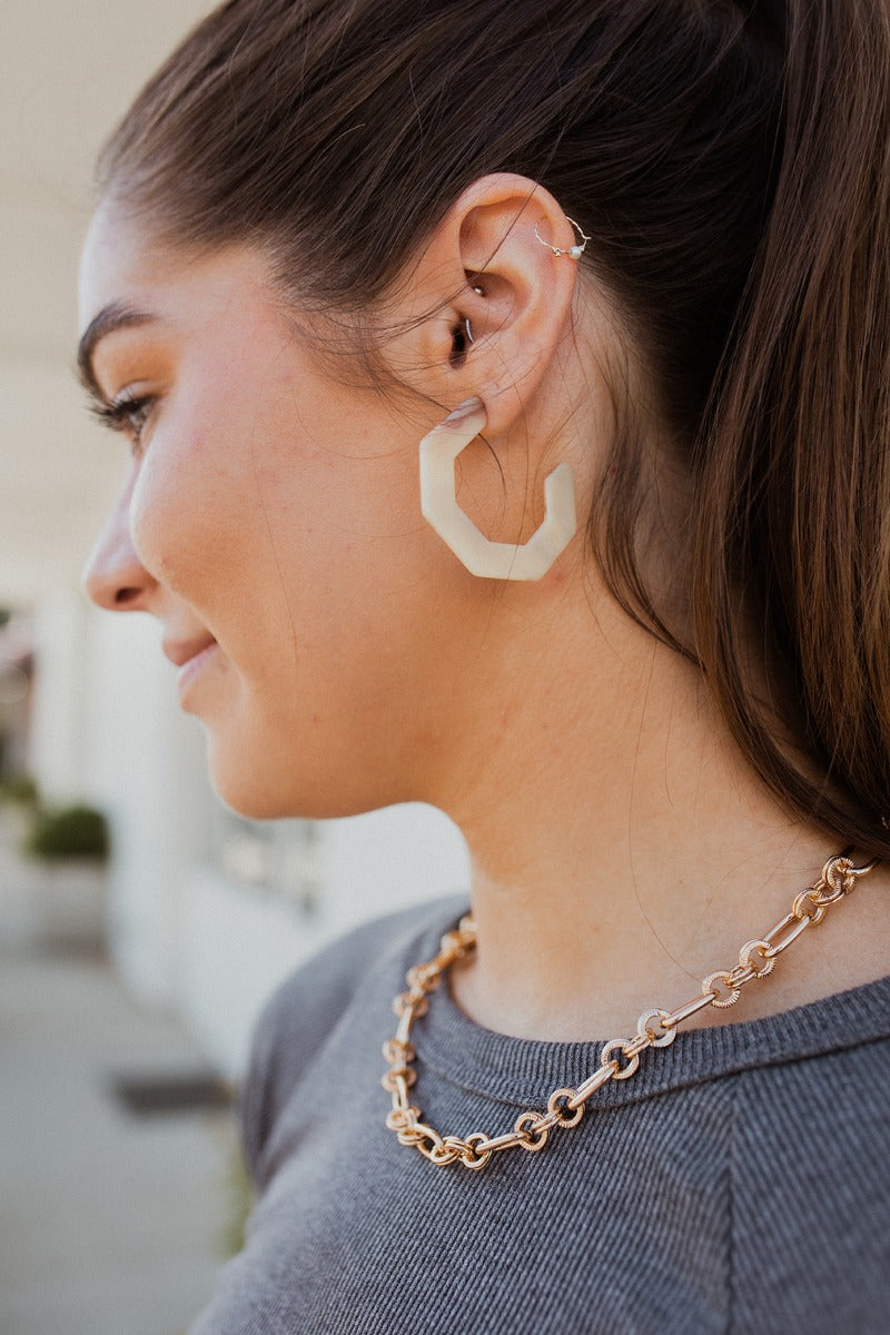 The On The Daily Earring is an ivory hoop style earring, featuring a hexagon shape with brown marbling through out.