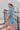 Back View of the Heading South Romper that features a blue colored material, a collar neckline, a short cuffed sleeve, a button-up front, two front pockets at the chest, a cinched waist, two side pockets, cuffed bottom hem, and two back pockets.