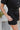 Side view of the Heading South Romper that features a black colored material, a collar neckline, a short cuffed sleeve, a button-up front, two front pockets at the chest, a cinched waist, two side pockets, cuffed bottom hem, and two back pockets.