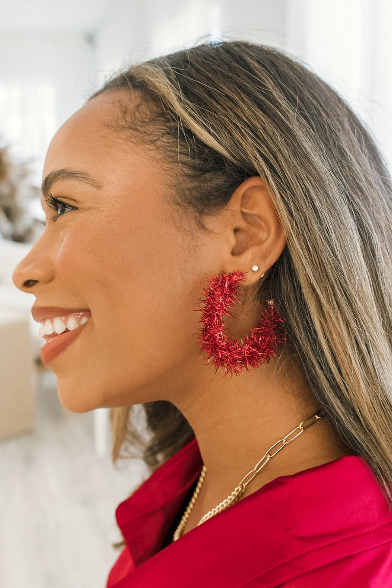 Side view of model wearing the You Give Me Joy Earrings in Red is a an open hoop style earring, featuring red textured frills.