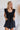 Frontal view of the End Game Romper that features a black cotton material, a rounded v neckline, a sleeveless design with tick straps, ruffle details at the straps, side pockets, a shorts bottom, a tie back, and a flowy fit.