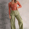 Full body front view of model wearing the Kimberly Olive Wide Leg Cargo Pants that have olive green denim-like fabric, brown contrast stitching, distressing, cargo pockets, a front zipper, belt loops, and wide legs.