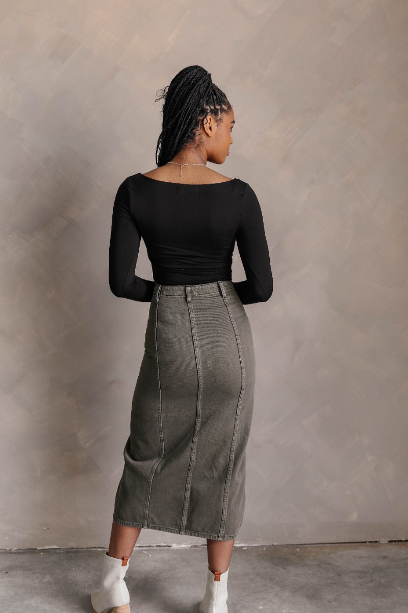 Back view of model wearing the Greta Black Basic Long Sleeve Crop Top that has black knit fabric, a cropped waist, a thick band hem, a square neckline, and long sleeves.