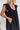 Frontal view of the End Game Romper that features a black cotton material, a rounded v neckline, a sleeveless design with tick straps, ruffle details at the straps, side pockets, a shorts bottom, a tie back, and a flowy fit.