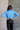 Back view of model wearing the Gabriela Blue Turtleneck Sweater that has blue knit fabric, ribbed hem, a turtleneck neckline, dropped shoulders, and long sleeves with cuffs.