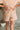 Lower back view of model wearing the Laguna Floral Romper that has denim fabric with an orange, pink, aqua, green and blue floral print, folded hem, two front chest pockets, side and back pockets, snap up buttons, a collared neck, and short sleeves
