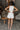 Full body back view of model wearing the Never Out Of Style Romper which features white fabric, side pockets, a sleeveless design, a round neckline, and a monochromatic back zipper with a hook closure.