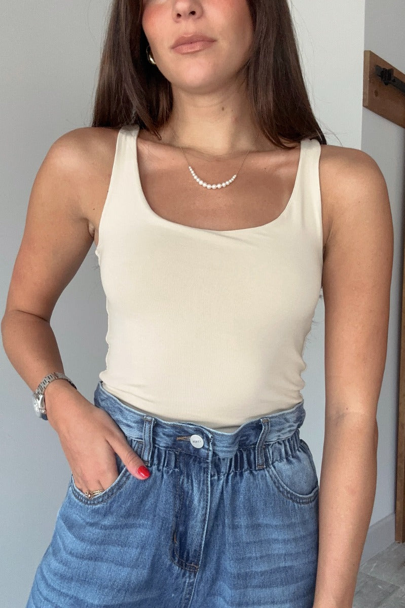 Front view of model wearing the Josie Beige Basic Scoop Neck Tank that has stretchy double-layered beige knit fabric, an elastic hem, a scooped neckline, and thick straps.