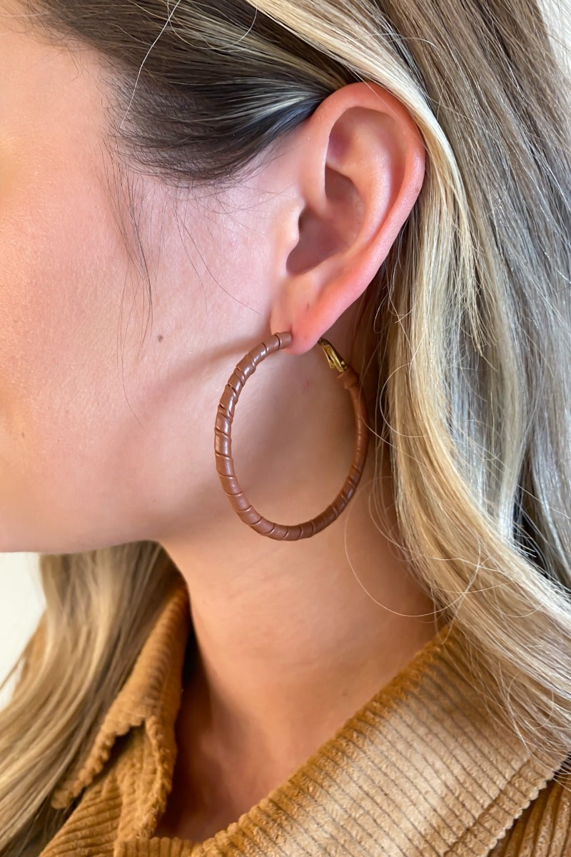 Close view of model wearing the What About Me Hoop Earrings that feature latch-back gold hoops wrapped with brown faux-leather material.