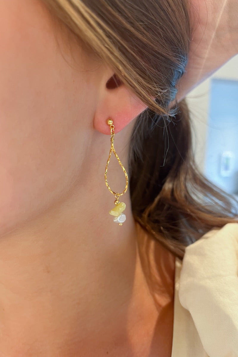 Close view of model wearing the Summer Fling Earrings that have a hammered gold tear drop shape with a white and yellow bead.