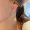 Close view of model wearing the Summer Fling Earrings that have a hammered gold tear drop shape with a white and yellow bead.