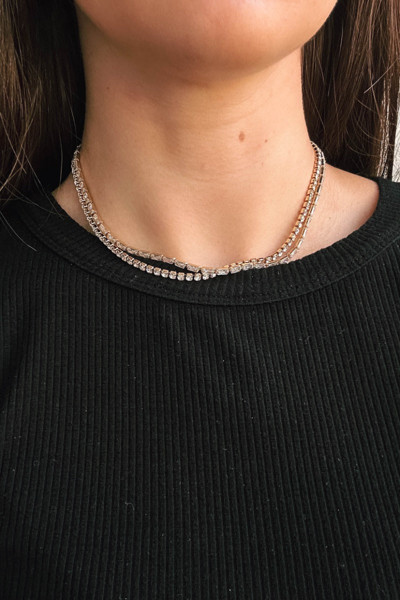 Close up view of model wearing the Aria Rhinestone Layered Necklace which features one layer with rectangle shaped clear stones and one layer of circular shaped clear stones set in gold.