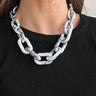 Front view of model wearing the Mya Grain Chain Link Statement Necklace which features oval shaped links, black, grey and white marble design and gold adjustable link closure.