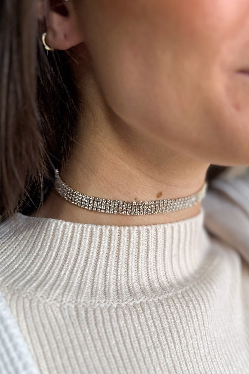 Close up view of model wearing the Aurora Rhinestone Chocker Necklace which features four rows of clear rhinestones set in gold and adjustable link closure.