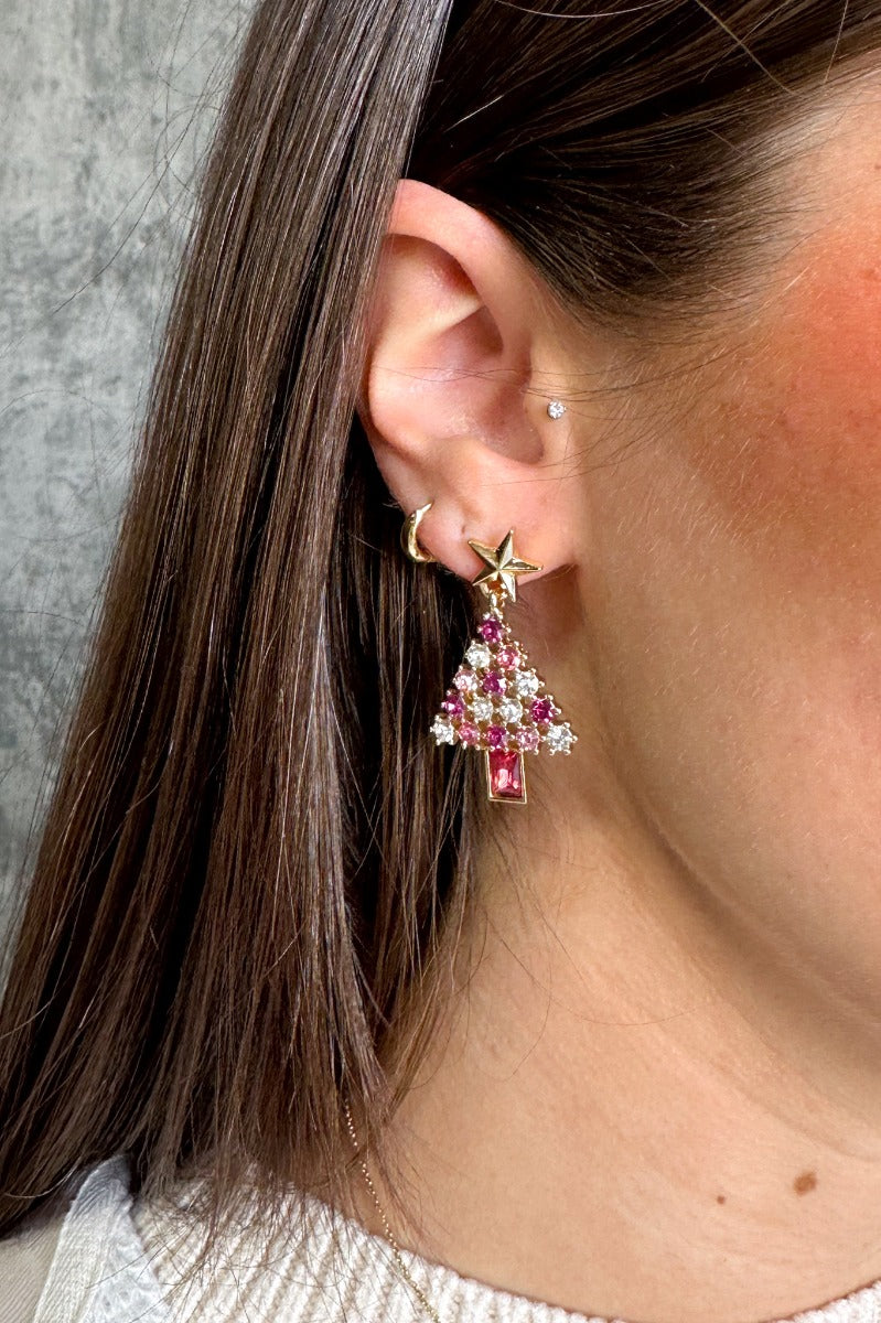 Close up view of model wearing the Pink Multi Christmas Tree Earring which features purple, pink and clearr stones shaped as a christmas tree with a gold star.