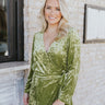 Front view of model wearing the Supernova Velvet Romper in Green, which has light green crushed velvet, a surplice neckline, a front skirt overlay with a side tie, and long fitted sleeves