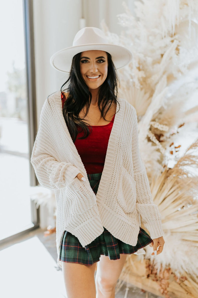 Front view of the Snow Cozy Cardigan featuring cream chenille fabric, cable knit pattern, two front pockets, side slits on the hem, and long sleeves with cuffs.