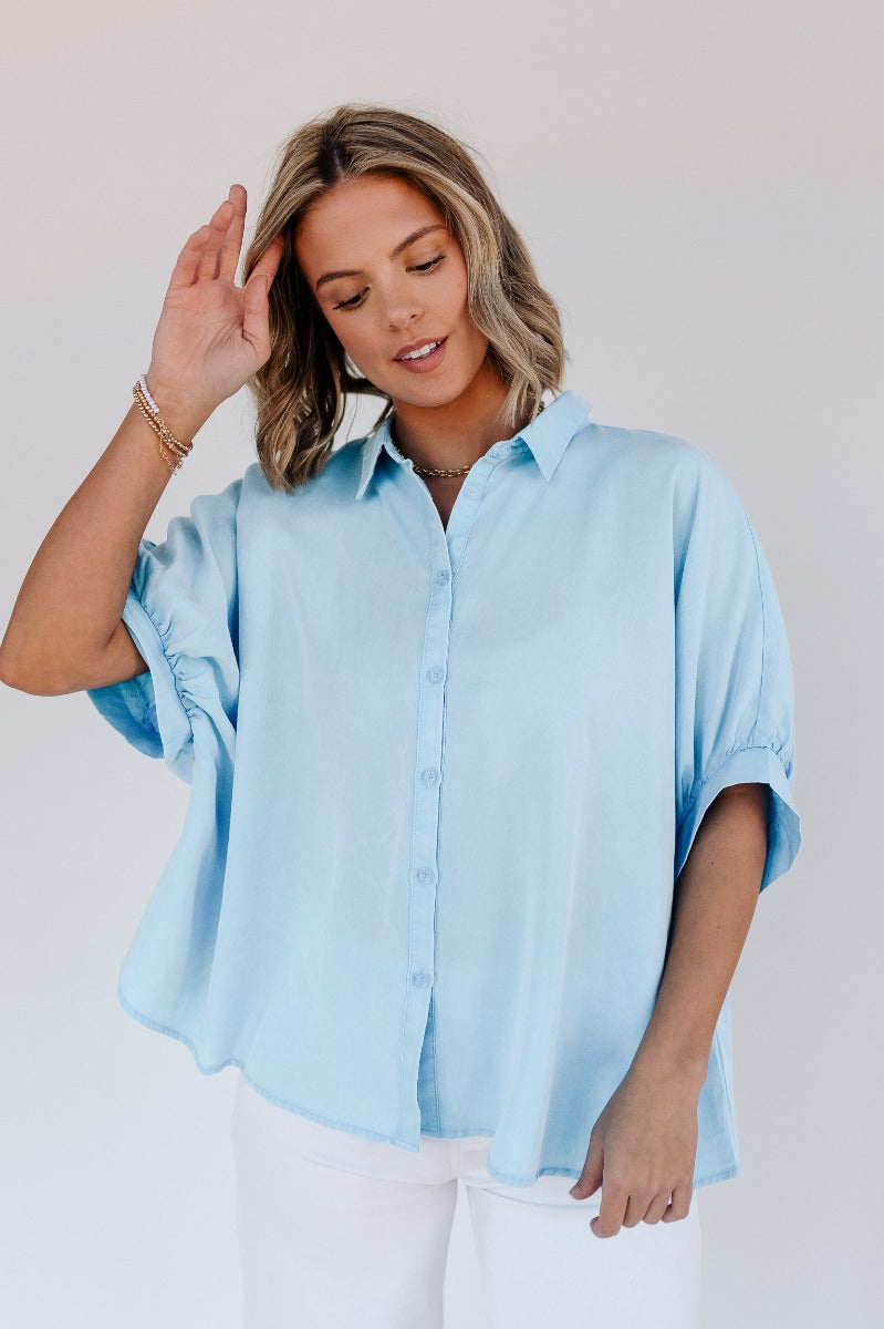 Front view of model wearing the Grace Washed Light Blue Short Sleeve Top which features light washed blue tencel fabric, monochrome front button up closure, collared neckline and short sleeves.