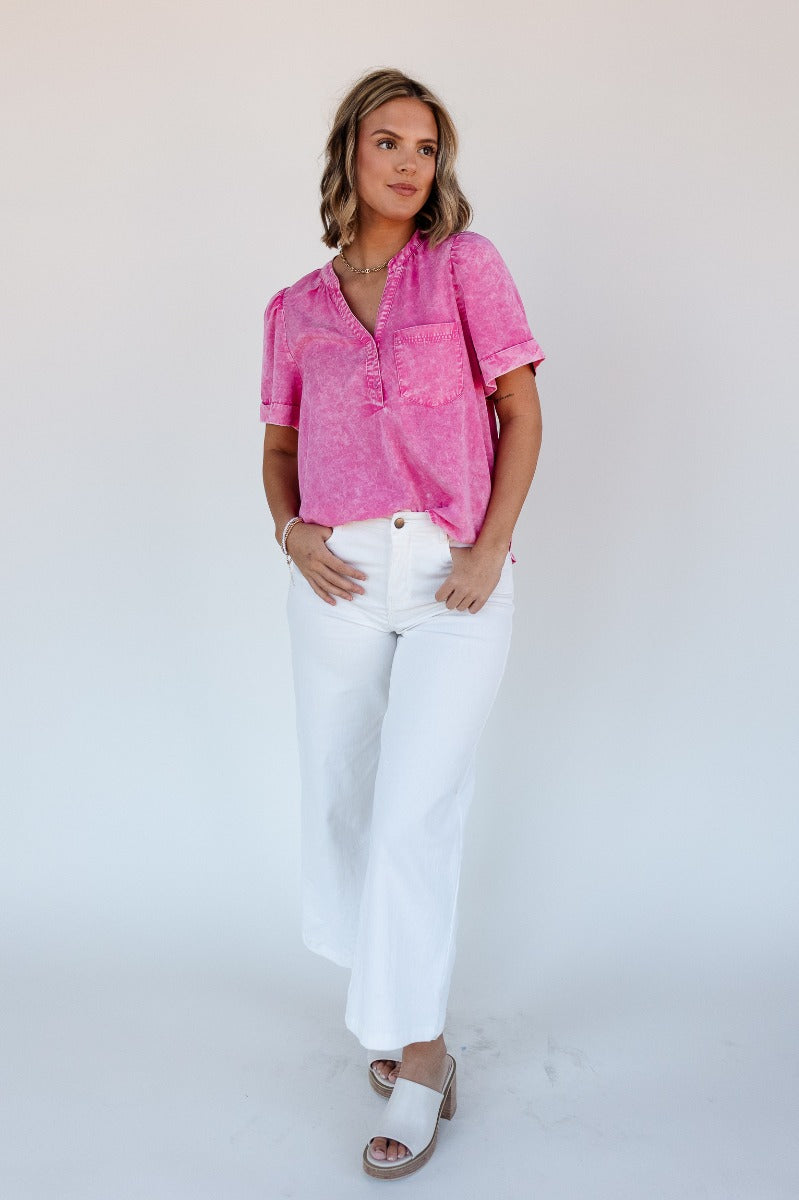 Full body view of model wearing the Ashlyn Washed Pink Short Sleeve Top which features washed pink tencel fabric, a scooped hem, a front left chest pocket, a monochrome quarter button-up v-neckline, and short sleeves.