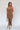 Full body front view of model wearing the Liliana Brown Asymmetrical Sleeveless Midi Dress that has light brown knit fabric, an asymetrical ruffle hem, midi length, square neckline, adjustable straps and sleeveless.
