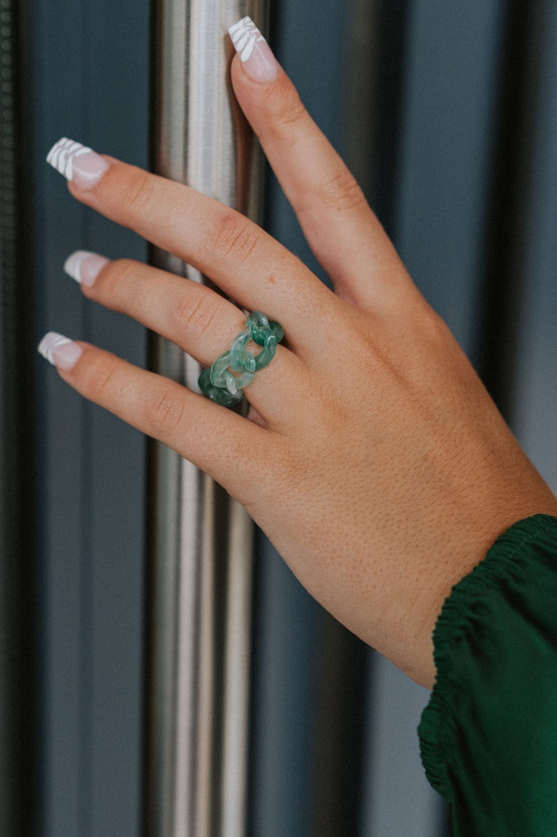 The Chain Reaction Ring Set features a set of four rings; three gold bands and a green, acrylic chain link ring.