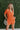 Frontal view of the Spur The Moment Denim Romper that features an orange denim material, a surplice neckline that snaps with a collar, half-length sleeves, a front zipper, pockets, pleating on the legs, and a 3" inseam.